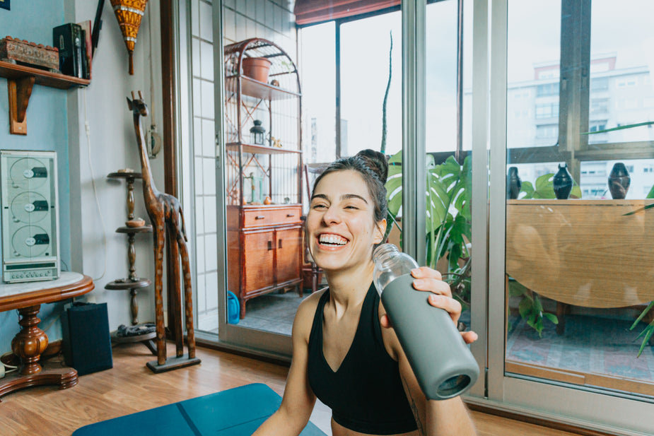 picture of a person laughing holding up a water bottle on a yoga mat